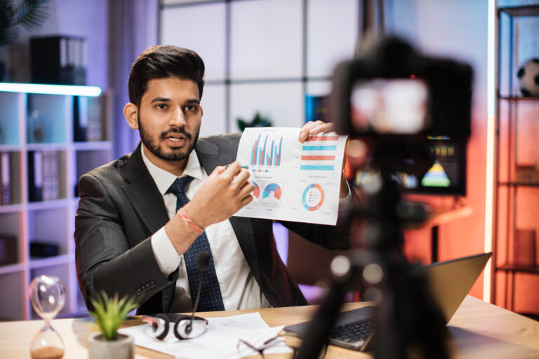 Arab businessman or broker in formal suit sitting in front of camera on tripod in evening office